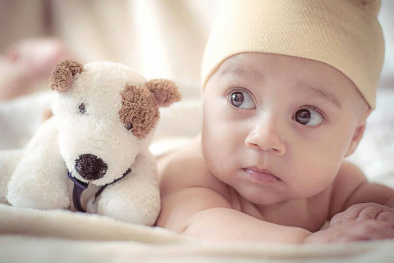 baby lying near dog plush toy